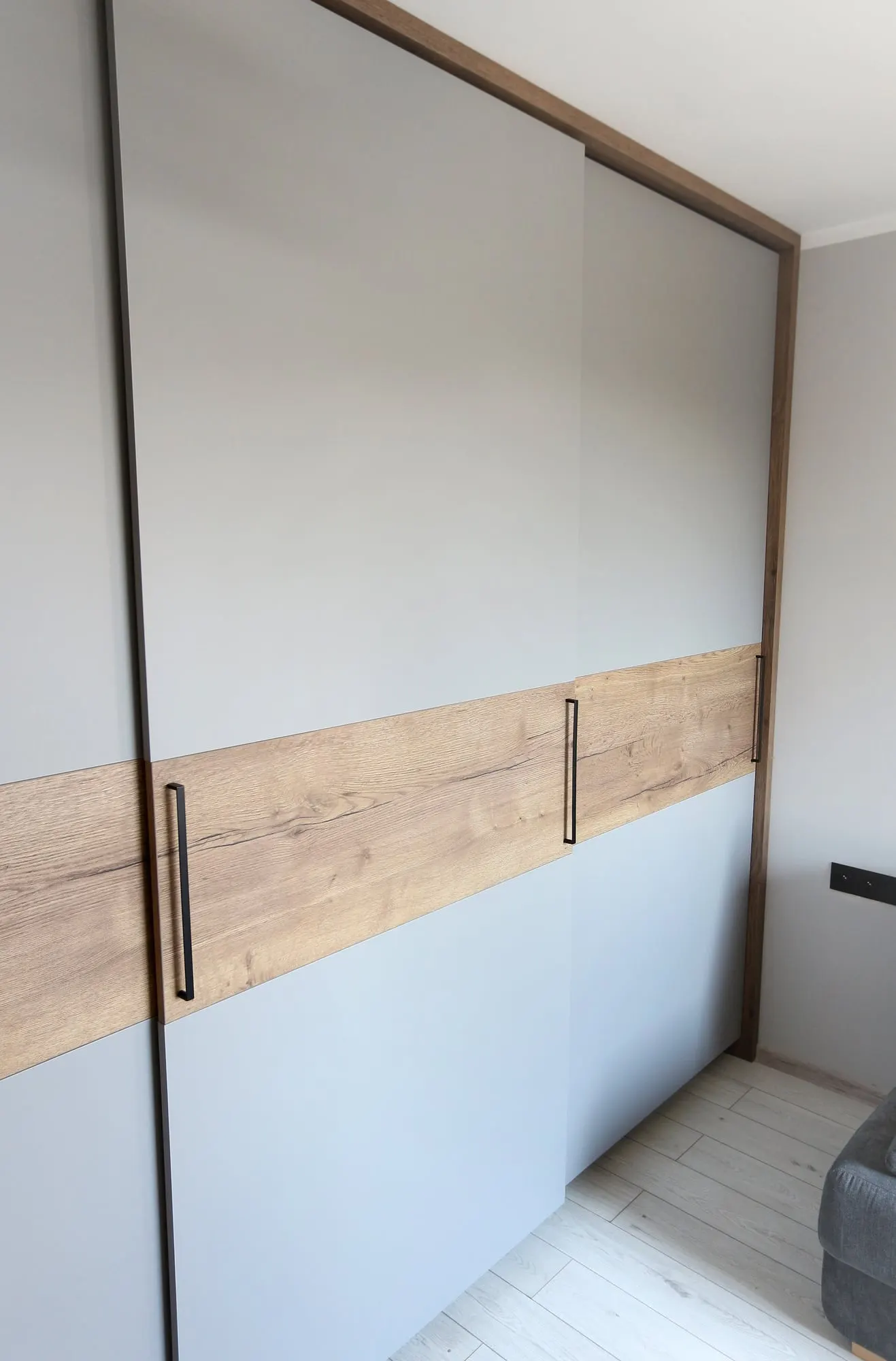 Szafa przesuwna pod kątem, w tle sofa i drzwi wejściowe do pokoju.