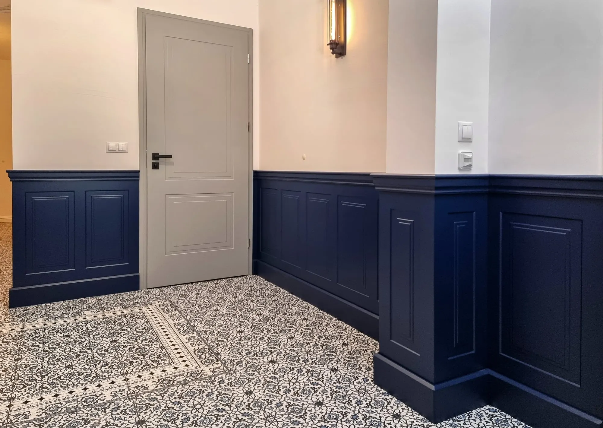 Korytarz z granatową boazerią na ścianach i wzorzystą, kafelkową posadzką.