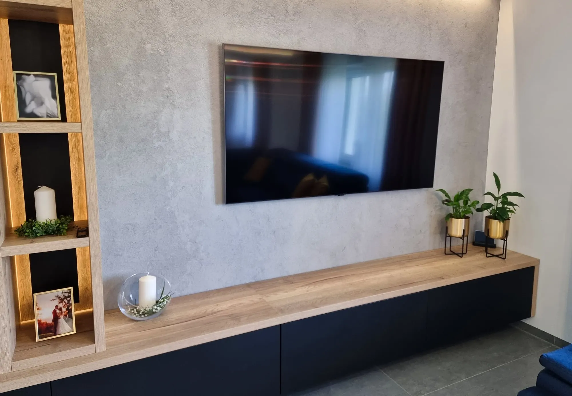 Ściana RTV z lamelowym panelem, otwartymi półkami i telewizorem nad czarną szafką.