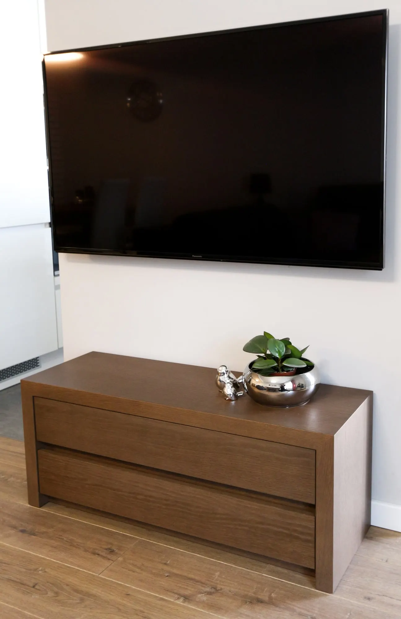 Telewizor nad niską szafką RTV w ciemnym dębie, z metalową dekoracją na blacie.