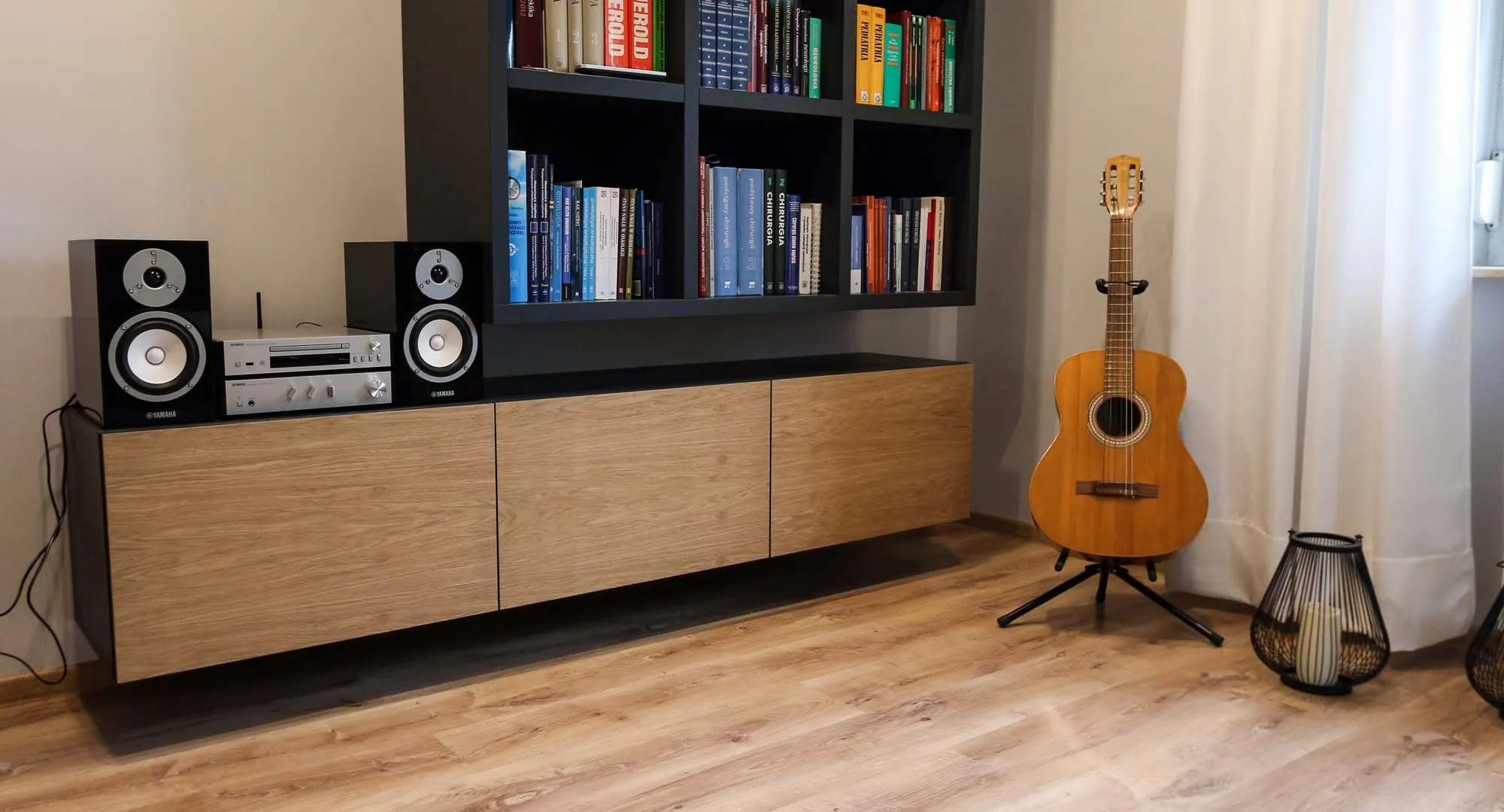 Zbliżenie wieży audio i gitary na tle regału z książkami i dębowej szafki.