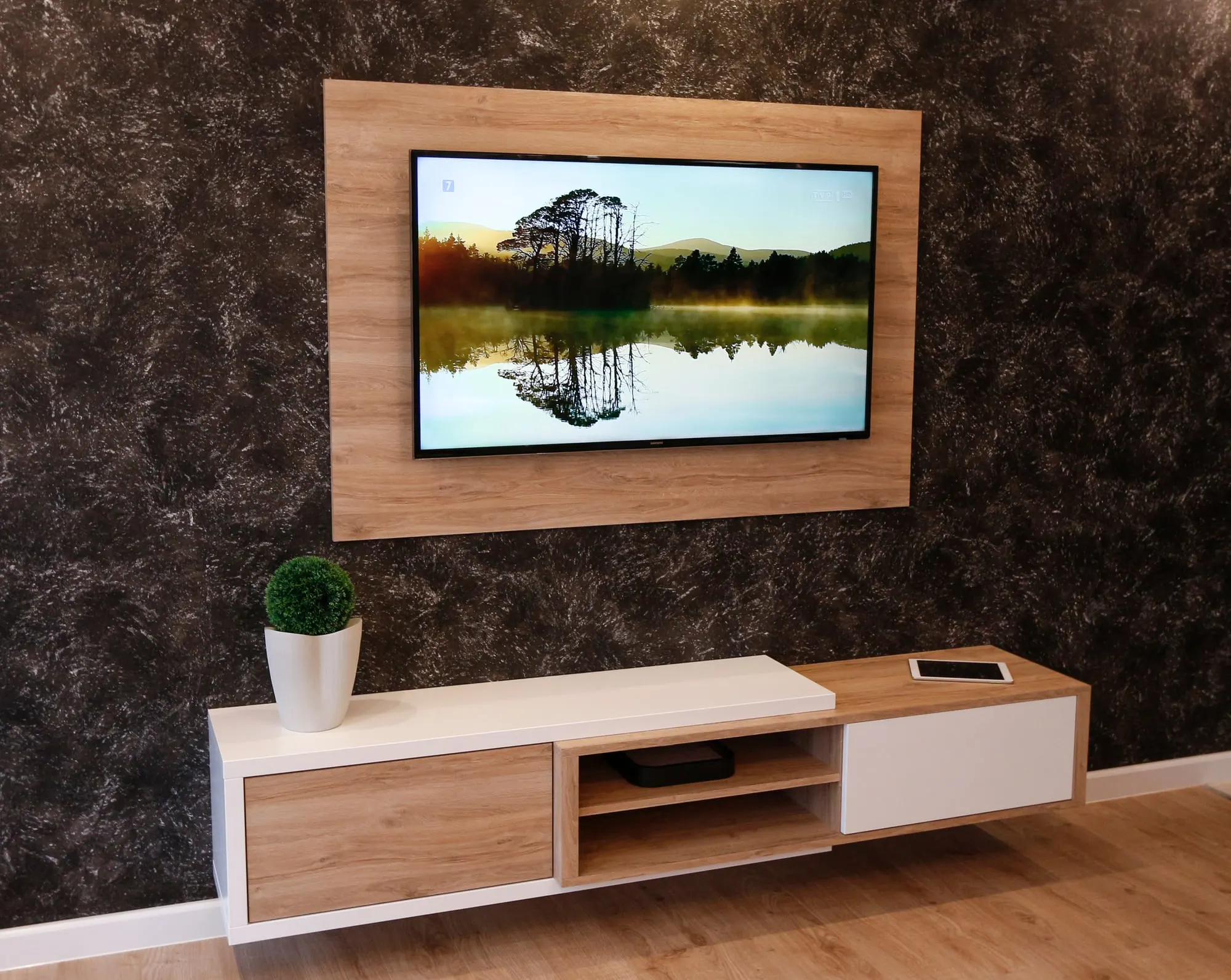 Inne ujęcie zabudowy RTV w dębie i bieli, z telewizorem i rośliną w donicy.