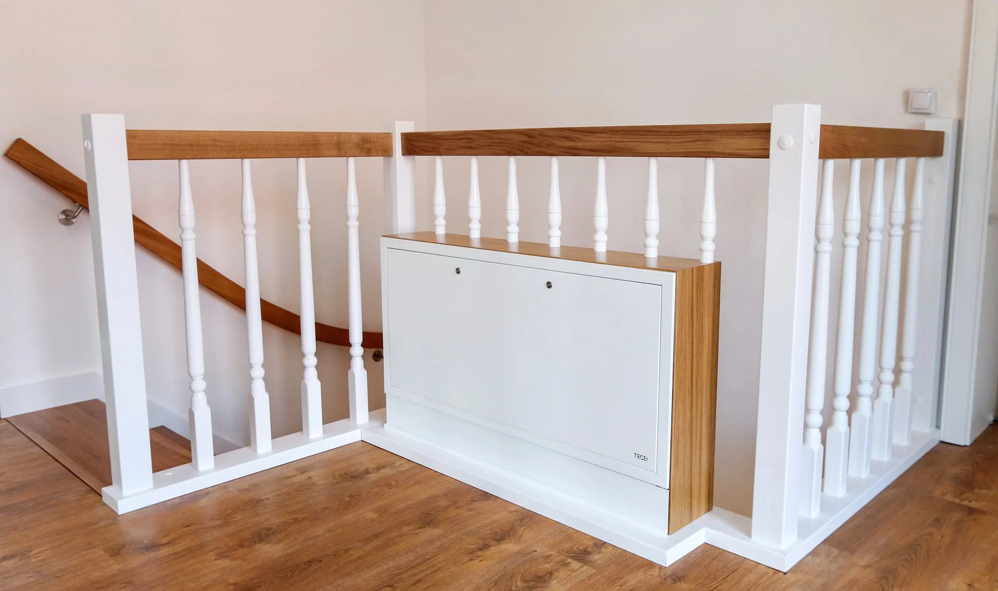 Górny bieg schodów z białą balustradą i wbudowaną szafką pod poręczą.
