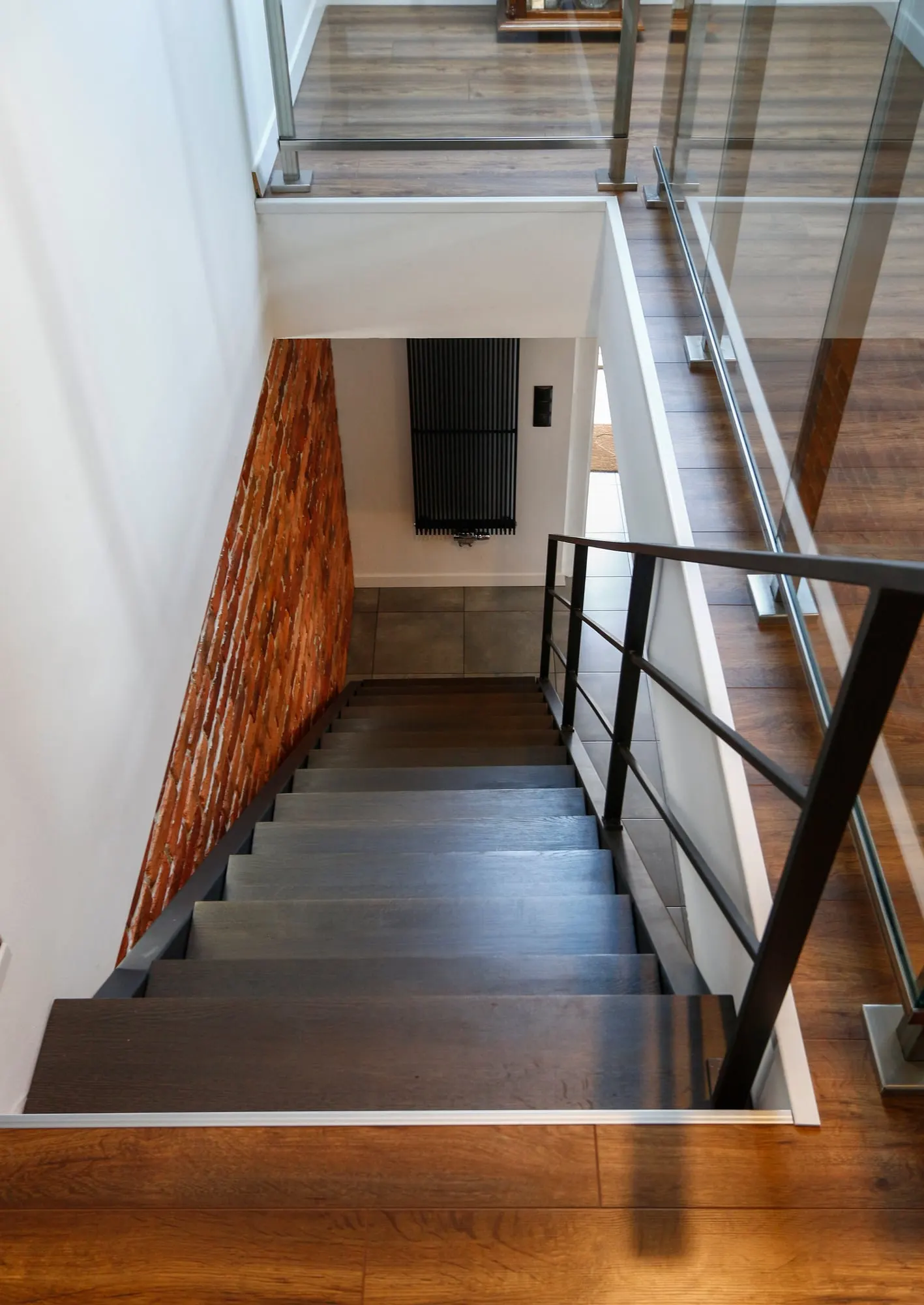 Widok schodów z góry, z przeszkloną balustradą i ciemną podłogą na dole.