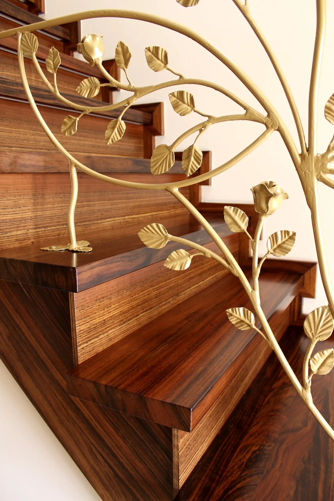 Zbliżenie na złotą, kutą balustradę o motywie liści na tle ciemnego drewna stopni.